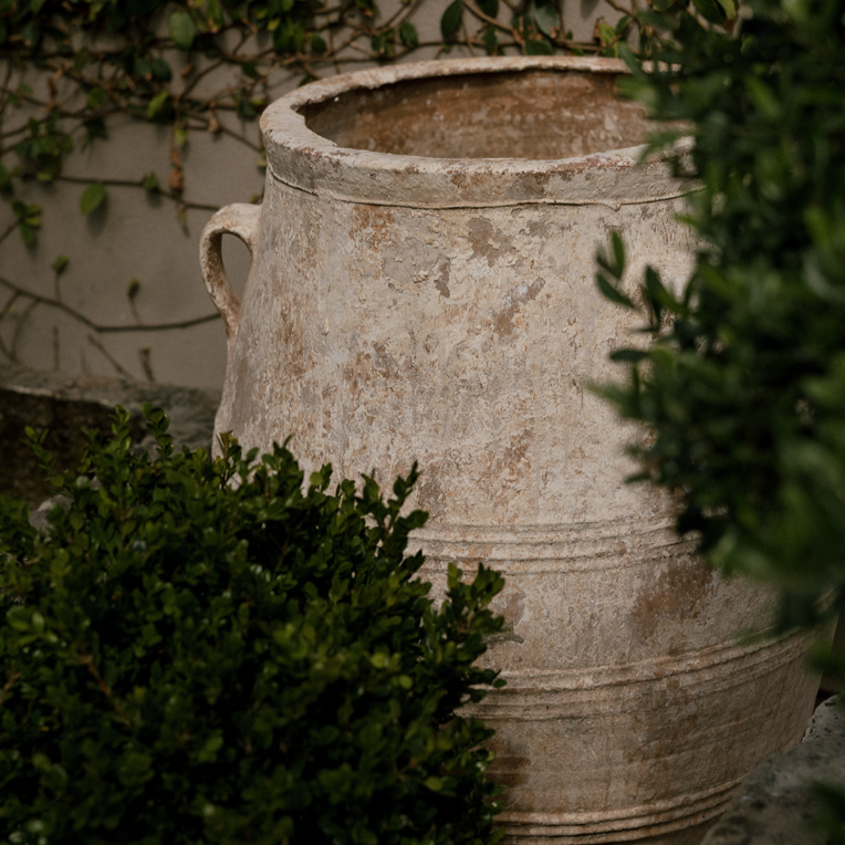 The Well by BDAntiques antique 3-handled terracotta olive jar with a weathered rustic finish in a garden setting.