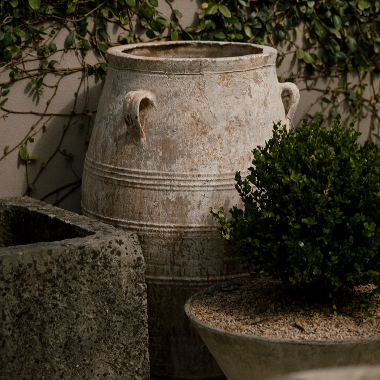 The Well by BDAntiques antique 3-handled terracotta olive jar with a weathered finish in a garden setting.