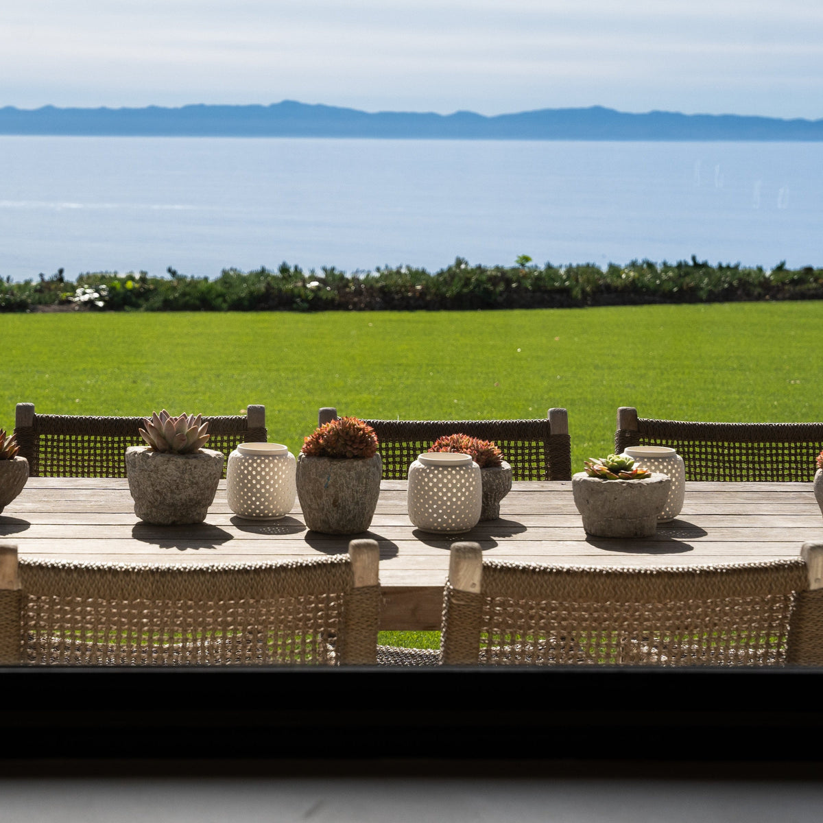 The Well by BDAntiques carved stone bowl planters with succulents on a wooden table overlooking a coastal landscape.