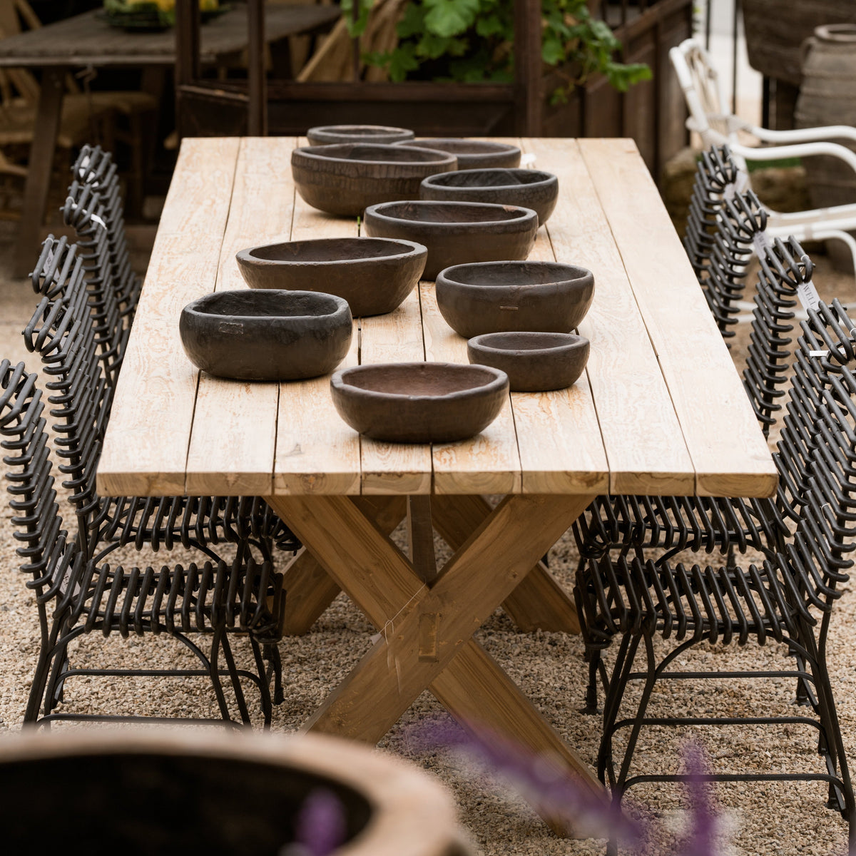 The Well by BDAntiques metal outdoor chairs with curved iron rod frames arranged around a rustic wooden dining table.