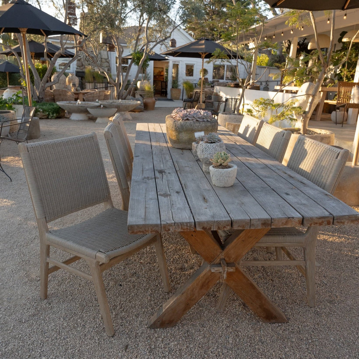 The Well by BDAntiques Sedona cushionless outdoor dining chairs with teak frames and resin wicker backs at a table.
