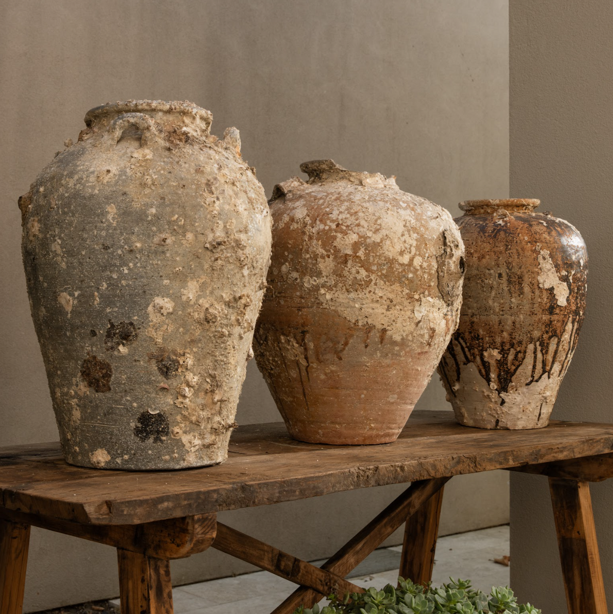 The Well by BDAntiques collection of three antique shipwreck pottery vases with weathered textures on a wooden bench.