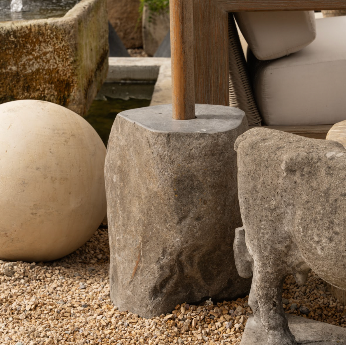 The Well by BDAntiques stone umbrella stand with a natural, rugged finish, providing a stable base in a patio garden.